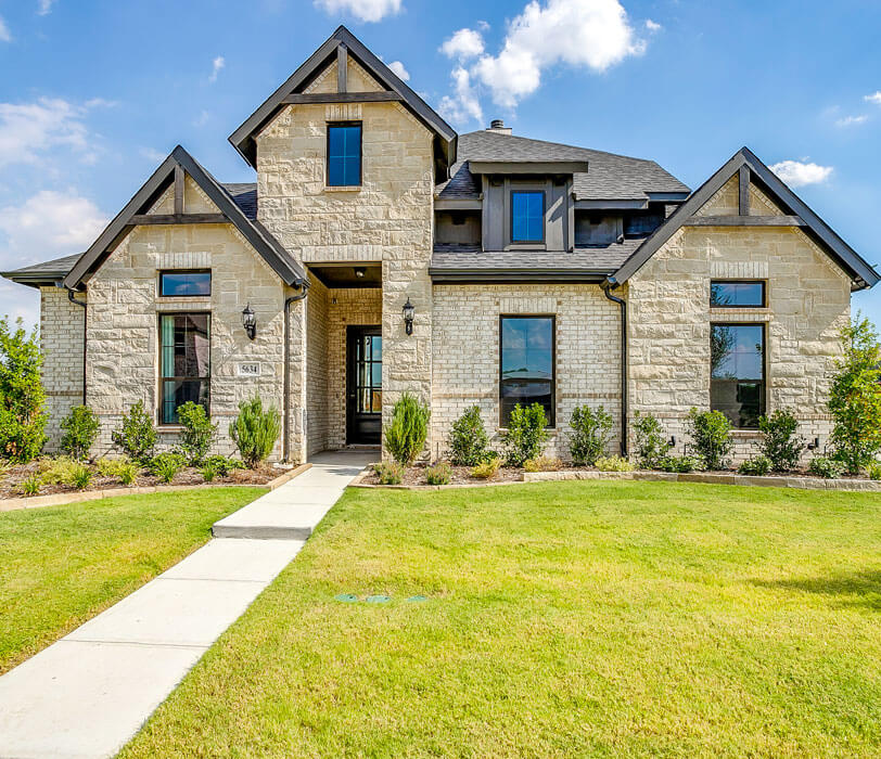 Two-story modern stone house in Redden Farms with black trim, large windows, and lush front lawn.