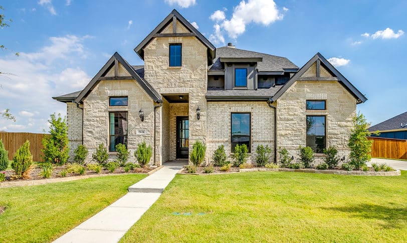 Two-story stone house in Redden Farms new home community with landscaped yard and gabled roof.