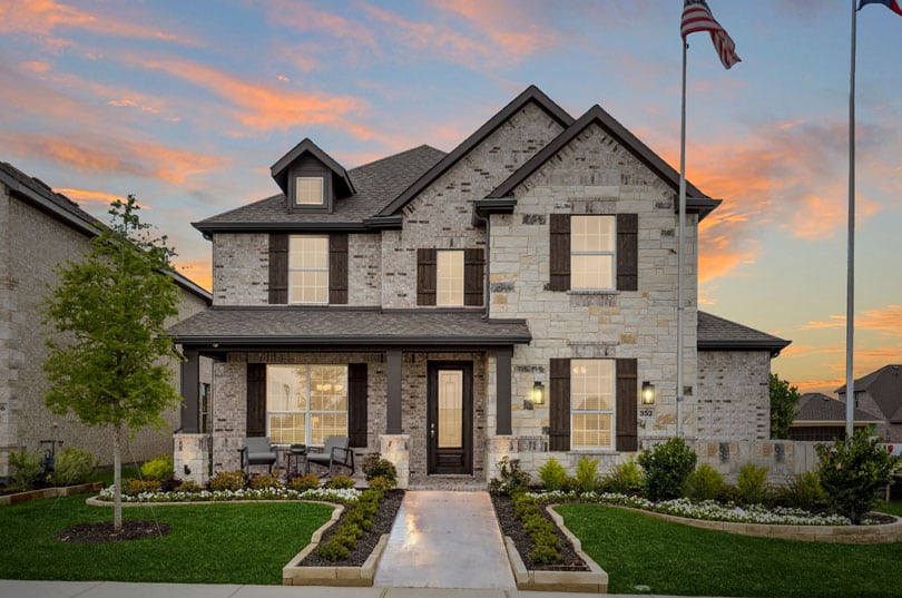 Two-story brick house in Redden Farms with porch, landscaped yard, and two flagpoles at sunset.